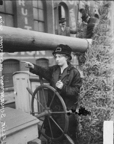 Elise Schunemann, at the steering wheel of the ship. Evergreen trees behind her.